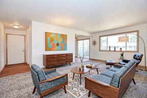 A living room with a blue couch, a chair, a coffee table, and a painting on the wall.