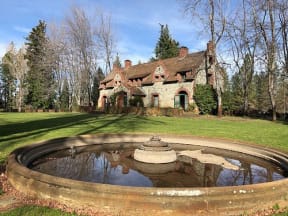 a fountain in the middle of a grassy area with a house in the background