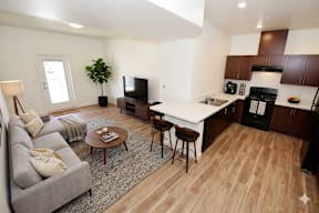 A modern living room with a grey sofa, a wooden coffee table, and a kitchen area in the background.