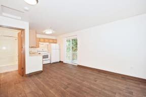 an empty living room with a kitchen and a door to a balcony