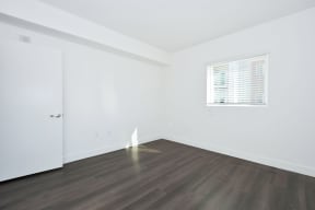 a bedroom with white walls and wood floors and a window