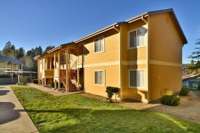 a picture of a yellow apartment building with a green lawn and blue sky in the background