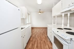 an empty kitchen with white appliances and wood flooring