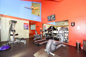 A gym with orange walls and a variety of exercise equipment.