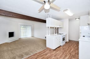 an empty living room with a kitchen and a ceiling fan