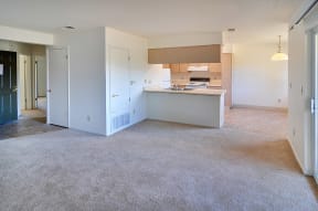 an empty living room with a kitchen in the background