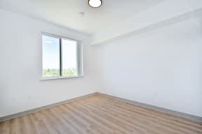 an empty bedroom with a window and hardwood floors