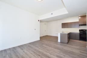 the living room and kitchen of an apartment with white walls and wood flooring
