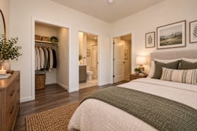 A bedroom with a large bed and a closet with clothes hanging.