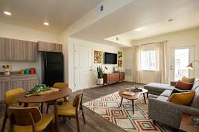 A living room with a grey couch, a wooden table and chairs, a black fridge, a flat screen TV, and a rug.