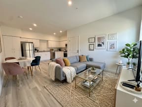 A modern living room with a grey sofa, a glass coffee table, and a television.