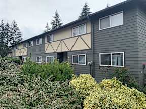 A grey building with a beige trim and windows surrounded by greenery.