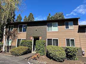 A building with brown siding and white trim is surrounded by green bushes.