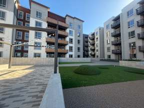 A modern apartment complex with a well-maintained lawn and walkway.