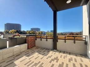A balcony with a brick pillar and tiled floor overlooks a cityscape.