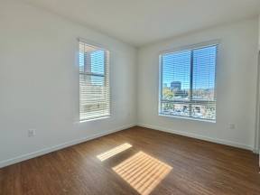 A room with wooden floors and two windows with blinds.