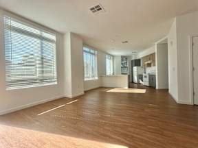 A spacious room with wooden flooring and large windows.