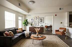 A living room with a grey couch, a brown armchair, a wooden coffee table, and a large window.