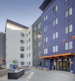 A playground area is located in front of a white building with a blue building to the right.