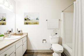 A white toilet sits in a bathroom next to a sink and a shower.