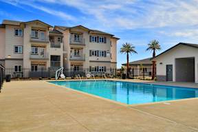 A swimming pool in front of a building with a fence and palm trees.