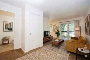 A living room with a couch, a coffee table, a television, and a window with a view of the outside.