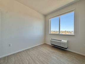 A room with a window overlooking a cityscape and a wall-mounted air conditioning unit.