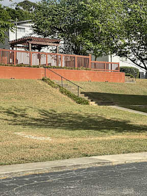 A red brick wall with a metal railing and steps leading up to a house.