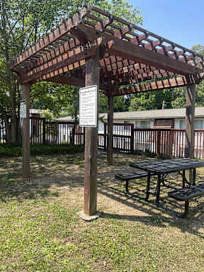 A wooden pergola with a sign and picnic table in the foreground.