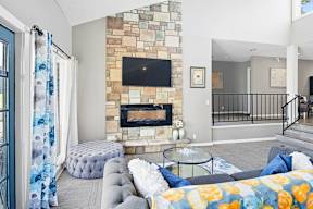 A living room with a stone fireplace and a grey couch.