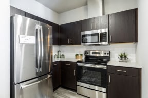 Kitchen with dark cabiets, stainless steel appliances, quartz countertops, and subway tile backsplash
