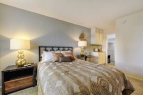 Model home bedroom with larger bed, side tables with decorative wall art. There is plush carpeting in the bedroom and built-in storage cabinets in the corner. 