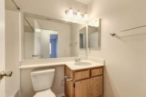 Vacant apartment home bathroom with sink and vanity.  Large mirror and bright lighting above the sink. 