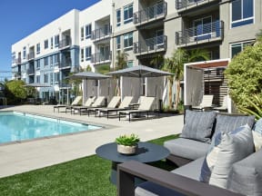 a poolside patio with chairs and a table in front of an apartment building