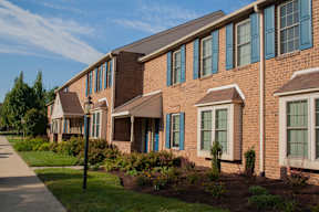 An exterior view of our Severgn's two-story brick apartment buildings with beautiful landscaping lining a sidewalk.