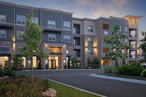 A modern apartment building with a driveway and landscaping in front.