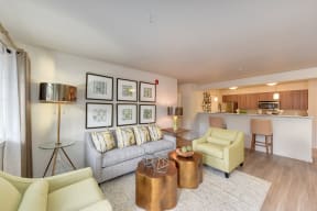 Model Living Room with Couch, View of Kitchen, White Sofa, Hardwood Inspired Floor, Lime Chairs, and Lamp on Glass Table