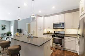 A modern kitchen with pendant and recessed lighting, a kitchen island, stainless steel appliances, and hardwood-style flooring near the living room. at Keva Flats, Exton, 19341