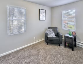Carpeted living space, with two windows on two walls. Staged with a chair and side table.at Woodhaven, Everett, WA 98203