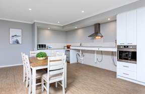 A modern kitchen with white chairs and a wooden table.