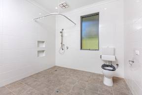 A white toilet with a grey seat in a white tiled bathroom.
