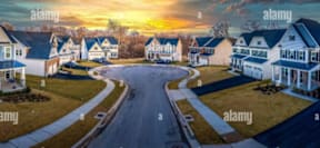 a painting of a street with houses and a sunset in the background