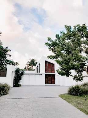 A white house with a red door and a tree in front.