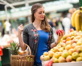 a woman holding an apple and a basket of fruit