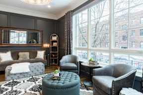 A living room with a grey couch, a grey armchair, a grey ottoman, and a black and white rug.
