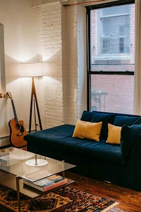 A living room with a blue couch and a guitar hanging on the wall.