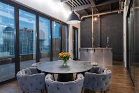 A round table with grey chairs and a vase of flowers in the middle.