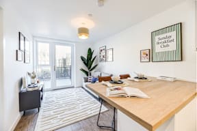 A dining room with a wooden table and chairs, a plant, and a sign that says "Sunday Breakfast Club".