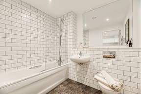 A white tiled bathroom with a bathtub, sink, and toilet.