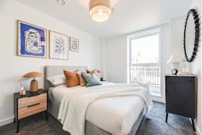 A bedroom with a large bed, a nightstand, and a window with a view of a balcony.